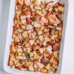 garlic and thyme potatoes in a white baking dish on a white table
