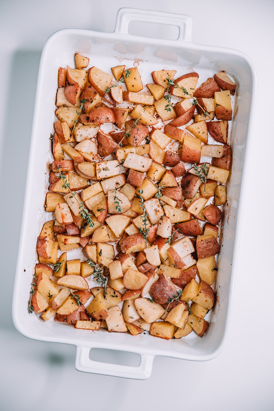 garlic and thyme potatoes in a white baking dish on a white table