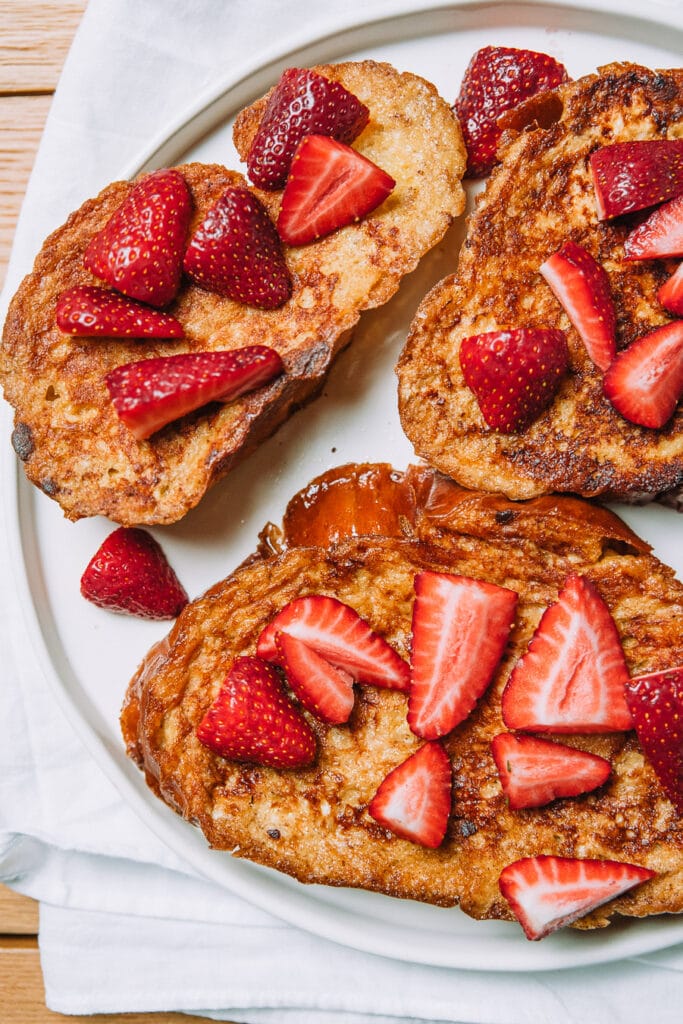 Fluffy slices of challah french toast topped with strawberries on a round plate