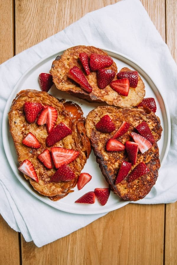 Thick luscious slices of French toast made with challah bread from the farmers market for easy homemade brunch topped with fresh strawberries. #brunch #frenchtoast #farmersmarket #strawberries