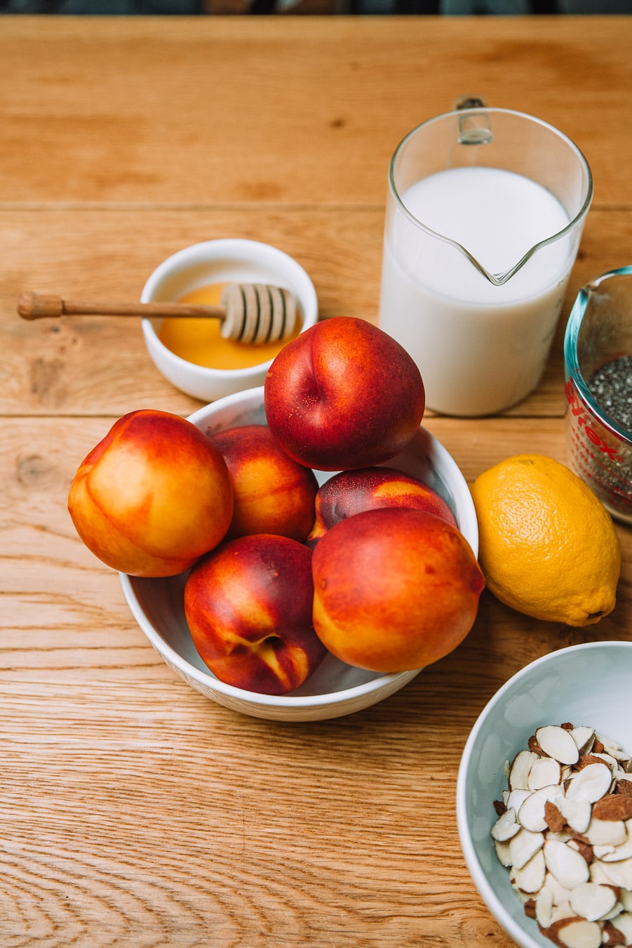 Milk, honey, lemon, almonds, chia seeds, and yellow nectarines in a bowl sitting on a wooden table