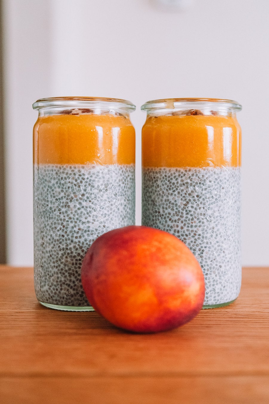 2 jars of nectar chia pudding with a nectarine on a wooden table. 