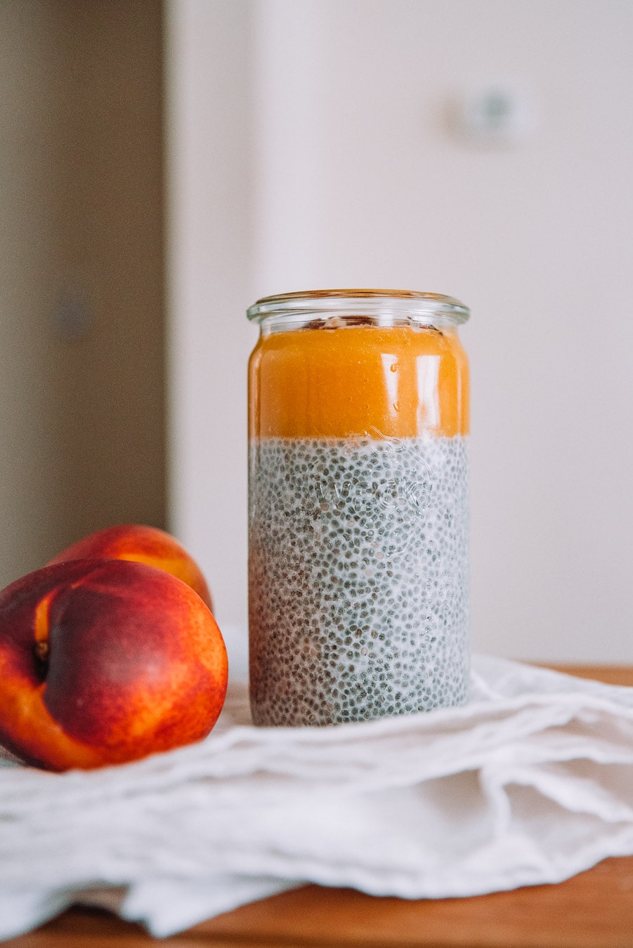 Jar of chia pudding with nectarines, a white table cloth, and wooden table. 