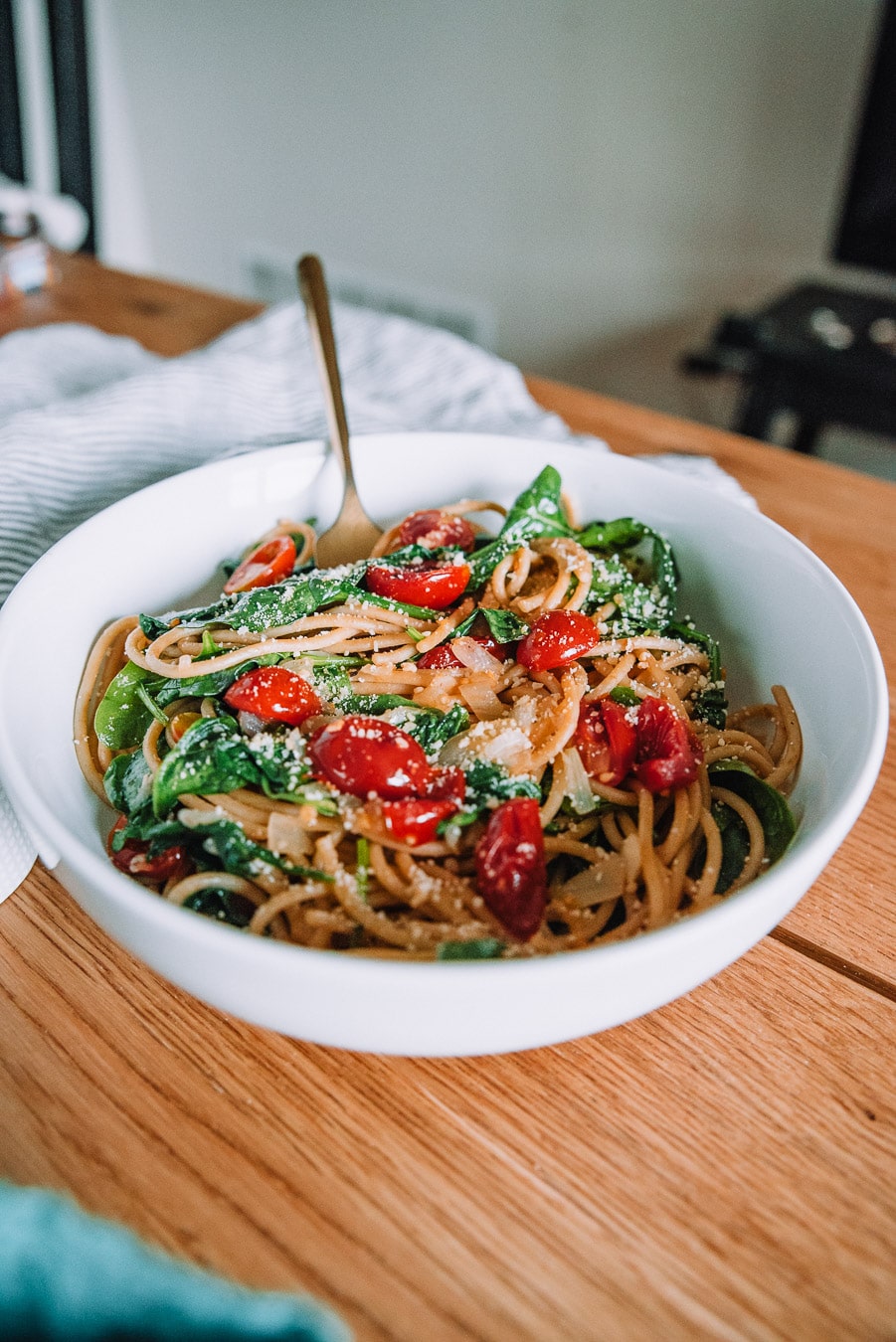White bowl with pasta and roasted cherry tomatoes and spinach. 